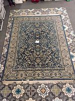 Top-down photo showing the full oriental area rug with detailed floral designs in blue, beige, and cream colors on a patterned floor surface.
