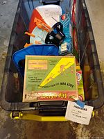 Plastic tub filled with multiple outdoor game items including plastic parts and boxed kits