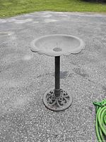 Black plastic bird bath on a cast metal stand showing flower-shaped basin and decorative base