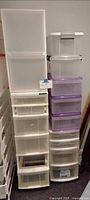Photo showing two plastic storage units side by side, one with white frame and clear drawers, the other with white frame and purple drawers.