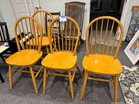 Four light wood Windsor back style dining chairs grouped together showing shape, finish, and condition.