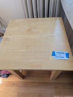 Top view of the light brown wooden end table showing natural wood grain and some minor scuffs or knicks on the surface.