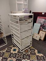 White metal wire frame shelving unit with five clear plastic drawers on a patterned carpet.