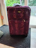 Exterior photo of the purple suitcase showing tiger stripe texture, zippered front compartment, wheels, and top handle.