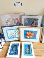 Six framed artworks displayed on floor showing a variety of coastal themed prints including fish, floral, lighthouse, mixed media.