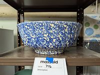 Side view of vintage ceramic serving bowl showing blue splatter pattern on cream background and flared rim with footed base on shelf.