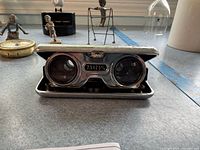 Close-up of 2.5x25mm folding opera glasses with blue trim, showing compact design and metal accents