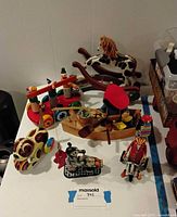 Photo showing a collection of vintage toys including a wooden toy set with colorful figures, a wooden rocking horse toy, tin clown toy, and musical toy figures arranged on a table.