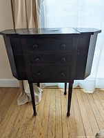 Front view of vintage dark brown wooden sewing table with three drawers and folding top closed.
