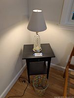 Full view of black wood side table, glass table lamp on top, and polka dot metal trash bin on floor