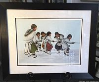 Framed and matted lithograph showing six Indigenous children playing tug-of-war in traditional winter clothing with snow ground background.
