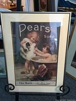 Full view of framed Pears soap poster with two children and a small puppy, mounted on black metal stand.