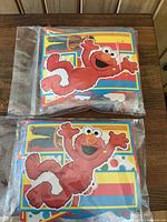 Two sealed Sesame Street themed party kits with colorful cutouts of Elmo and Big Bird in transparent packaging on a wooden surface