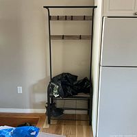 Full view of the entryway hall tree showing the bench seat with shoe rack underneath and multiple hooks above, as well as black metal frame and wood composite panels in natural wood finish.