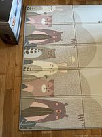 Photo of the play mat unfolded showing the cartoon animal side with various animals like bear, owl, rabbit, cat in pastel colors.