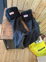 Pair of black boot socks/liners laid on wooden table, showing knit cuffs with Hunter logo patches.