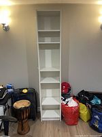 Straight-on front view of tall white bookshelf showing six shelves, standing in room beside various items.