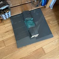 Top-down view of the square grey IKEA Lack table top on a wooden floor with four black legs bound together lying on top.