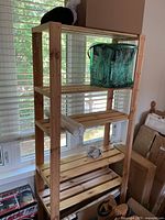 5-shelf pine wood shelving unit against window, partially loaded with some personal items.