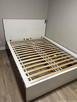 White full size platform bed frame with natural wood slats and headboard photographed in corner of room on wood floor