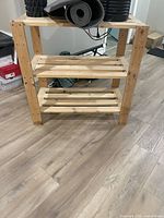 Front view of natural light wood 3-shelf shelving unit with slatted shelves on laminate flooring, showing sturdy build and screw details.