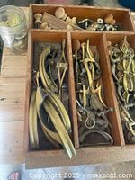 Top view of drawer divided into compartments containing brass and metal drawer pulls and handles of various shapes and sizes