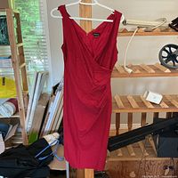 Front view of red sleeveless sheath dress with v-neck hung on white hanger showing fit and design details.
