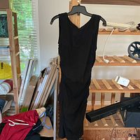 Front view of sleeveless black dress hanging on a wooden hanger, showing fitted shape and V-neck.