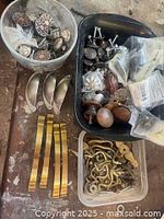 Various mixed metal drawer knobs and pulls including decorative round knobs, smooth pulls, and brass handles arranged in bins and containers.