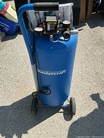 Front view showing upright blue tank with Mastercraft logo, handle and wheels