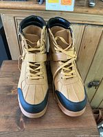 Front view of men's tan high-top boots showing synthetic upper, black toe cap, lace-up closure with strap.