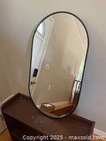 Front view of the oval wall mirror showing full reflective glass and black metal frame. Shows medium to large size and clean reflective surface.