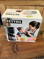 Front side of the branded box showing PCTTOIL food storage containers with lids and a person feeding a child.
