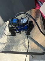 Photo showing Power Fist branded 12V air compressor unit with analog pressure gauge and attached power cord wrapped around compressor body.