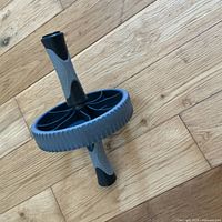 Full view of the gray and black ab roller wheel placed on wooden floor, showing the single wheel with rubber tire and handle grips.