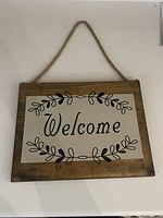 Front view of wooden welcome sign showing text, leaf accents, and rope hanger.