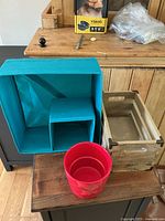 Photo showing turquoise fabric storage organizer, wooden crate, and red plastic bucket.