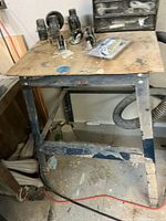 Work table with metal frame and wooden top with some stains and scratches, showing wear from use.