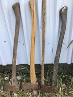 Three vintage axes standing upright against a metal wall showing wooden handles and rusted axe heads.