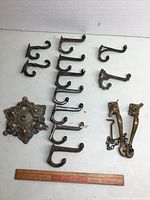 Full assortment of cast iron coat hooks and brass handles laid out with ruler for scale.