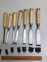 Set of seven wood chisels with wooden handles, brass ferrules, steel blades marked MOB FRANCE, and black protective plastic caps, displayed with a ruler for size reference.