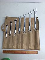 Six Craftsman combination wrenches arranged in size order on a tan cloth tool roll on a white surface with a ruler for scale.