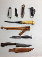 Overview of seven knives including folding knives, fixed blades, and accompanying leather sheaths.