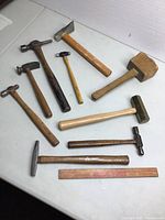 Photo showing the full lot of 10 assorted hammers and mallets including brass mallet, carving mallet, and other steel hammers arranged on table.