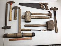 Full view of all hammers, mallets, and saw laid out on a white surface showing condition and variety of tools.