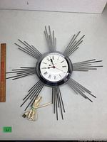 Full view of the starburst clock showing chromed metal rods and attached power cord.