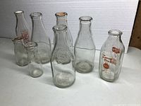 Eight assorted vintage milk bottles varying in size, shape, and labels, cleaned and free of chips.