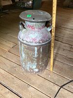 Photo showing front side of the metal milk can marked 'GEORGIAN BAY' with rust and paint wear, beside a measuring stick for scale.