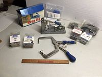 Overview of all items including Kreg Jig drill jig, clamps, screws, plugs, and box on a white table next to a wooden ruler for scale