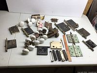 Full lot overview on white surface showing all porcelain knobs, hinges, lock boxes, strike plates, and metal door hardware.